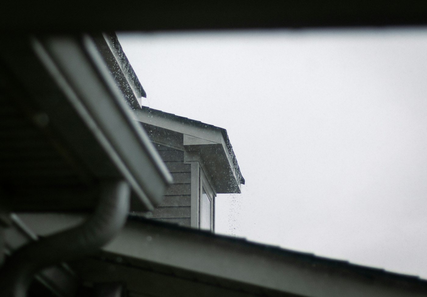 House roofline with a gutter and downspout against a gray sky